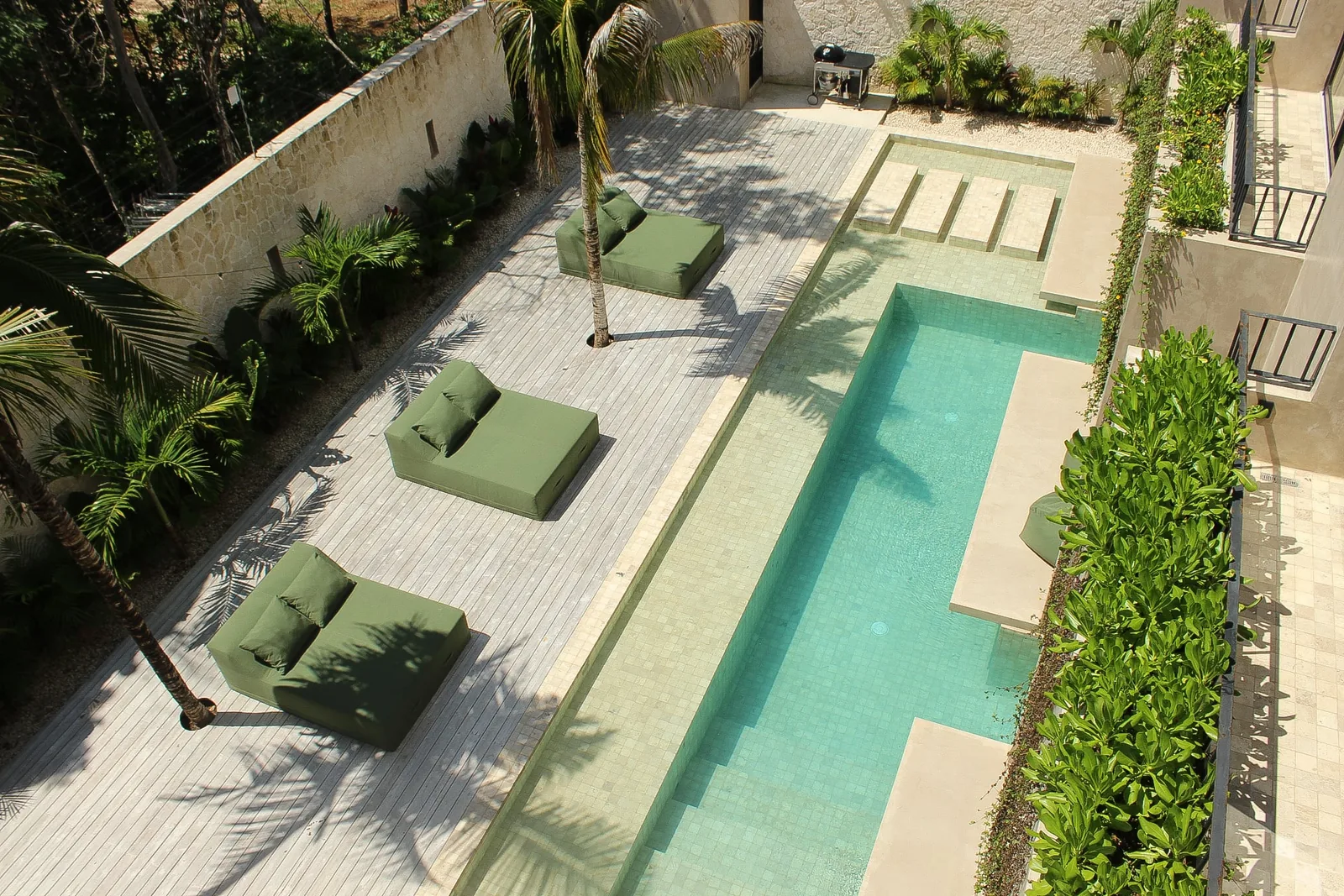Vista aérea de la alberca a nivel de jardín de Casa Uulum, su terraza y el jardín tropical